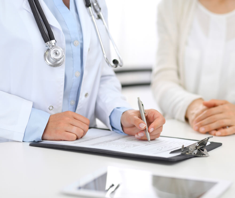 Doctor and female patient discussing something while standing near reception desk in emergency hospital